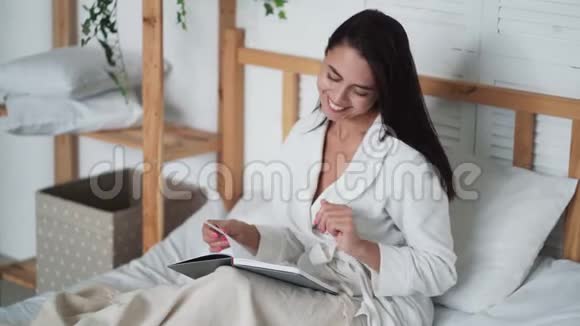 穿着白色浴袍的年轻美女躺在床上看书视频的预览图