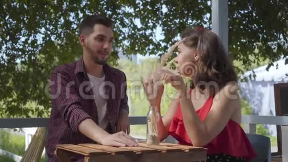 年轻的幸福夫妇坐在户外的小桌子旁互相交谈和微笑积极的男人和女人视频的预览图