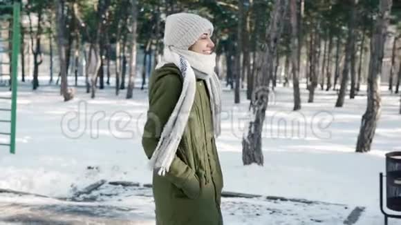 慢镜头描绘美丽快乐微笑的年轻女子穿着温暖的冬衣在白雪皑皑的冬公园里嬉戏视频的预览图