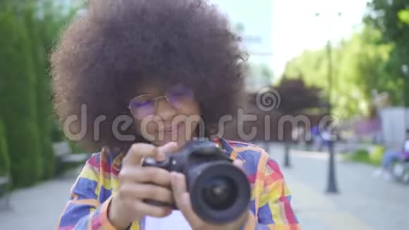 非洲女性发型是非洲式的摄影师在城市景观上带着相机看着相机微笑着视频的预览图