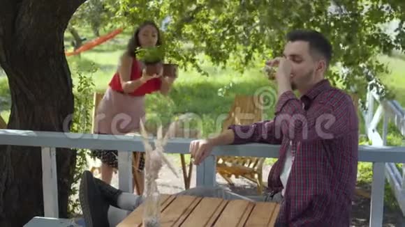 留胡子的男人在前面喝茶而穿着复古衣服的迷人女孩则在花盆里种花视频的预览图