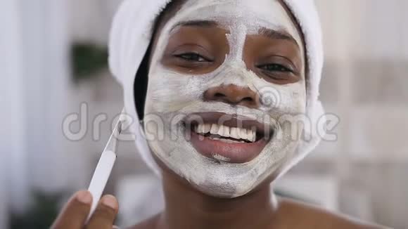 把头上戴着白毛巾的非裔美国女孩贴在脸上在白色的房间背景下微笑视频的预览图