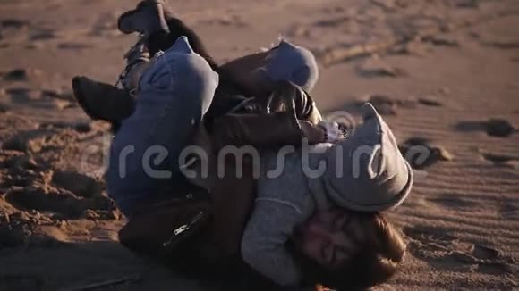 快乐年轻的妈妈穿着秋装躺在沙滩上快乐地拥抱着她的孩子把她抱起来视频的预览图