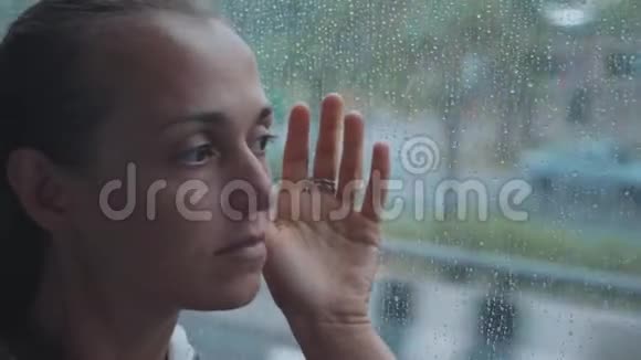 年轻悲伤的女人在乘公共汽车旅行时看着潮湿的窗户的肖像视频的预览图