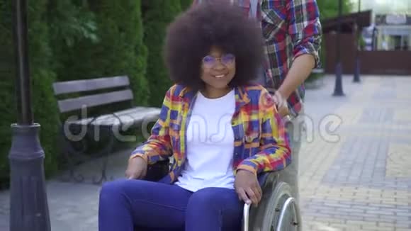 有非洲发型的非洲女人坐轮椅在公园里散步和一个朋友在一起玩得很开心视频的预览图
