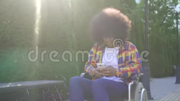 一位发型为非洲裔的美国女性轮椅上的残疾人使用智能手机阳光明媚视频的预览图