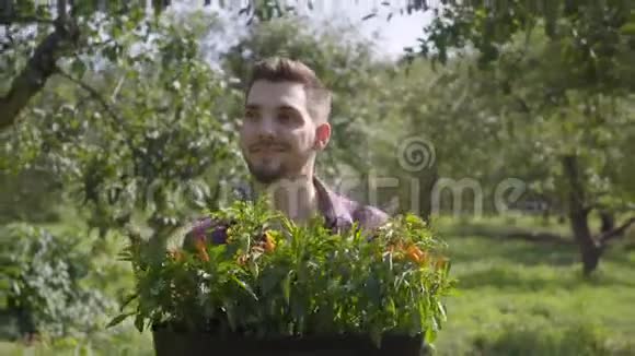 年轻微笑的胡子农夫手捧一壶花走过夏天的花园的肖像概念视频的预览图