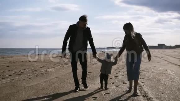 现代年轻的父母带着儿子走在中间正走在秋天春天的海边把手举起来视频的预览图
