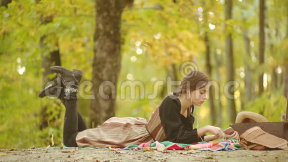 快乐的女人潮人在秋天的背景下在智能手机上听音乐公园里的女模特年轻女性喜欢玩视频的预览图