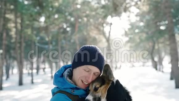 温暖的冬衣中快乐的人的情感肖像在寒冷的阳光下在白雪皑皑的冬公园里抚摸他的宠物视频的预览图