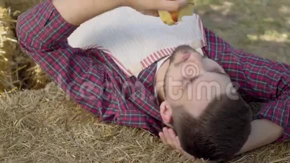 大胡子的年轻人躺在干草上吃新鲜的苹果农夫下班后休息乡村生活方式乡村风格视频的预览图