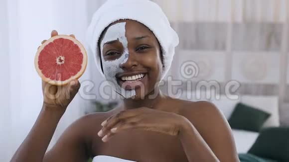 美丽的非洲裔美国妇女头上戴着白色毛巾脸前捧着半个多汁的葡萄柚视频的预览图