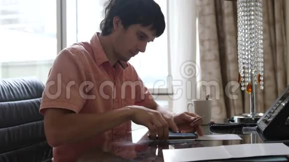 年轻的快乐男人坐在办公桌前通过互联网从智能手机上的银行卡支付在线支付视频的预览图