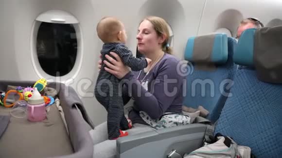 妈妈带着一个快乐的小孩子在飞机上一个女人把婴儿抱在怀里拥抱和亲吻她视频的预览图