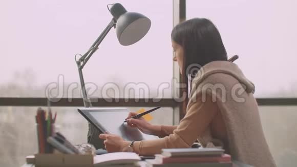 一个年轻的设计师女孩在一个有大窗户的办公室里使用一个工作站绘制现代图形屏幕创建标识视频的预览图