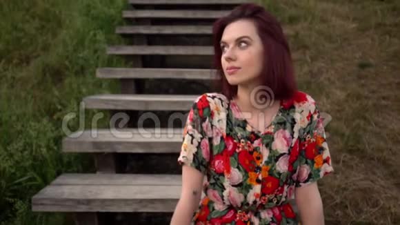 年轻漂亮的红发女郎坐在公园的木楼梯上视频的预览图