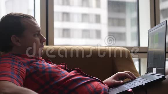 胖子坐在现代客厅的沙发上用笔记本电脑工作在家喝咖啡视频的预览图