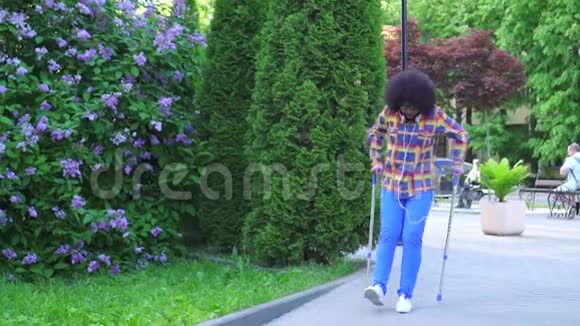 非洲女人头发是非洲发型穿着衬衫拄着拐杖断了腿走在街上慢悠悠的视频的预览图