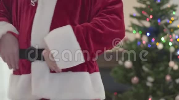 穿着圣诞老人服装的白人老人抱着他的肚子在圣诞树前跳舞幸福的概念视频的预览图