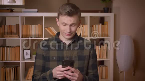 一位年轻迷人的白种人男学生的特写镜头他在电话里发短信看着摄像机微笑着视频的预览图
