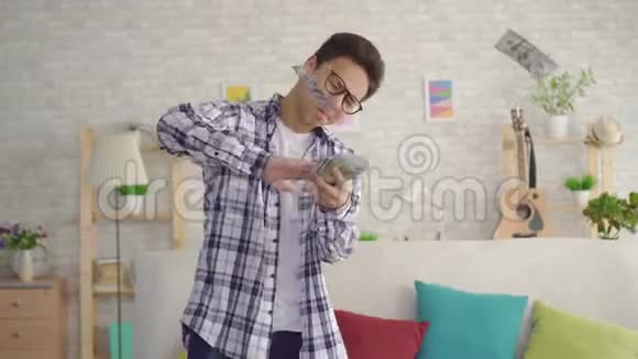 积极的亚洲年轻人带着眼镜在客厅里扔钞票视频的预览图