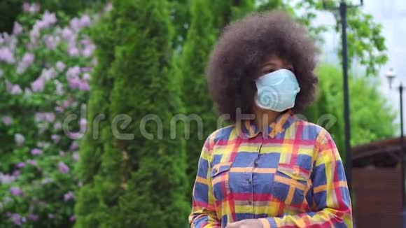 美国黑人妇女留着非洲发型戴着医用防护面具手里拿着智能手机视频的预览图