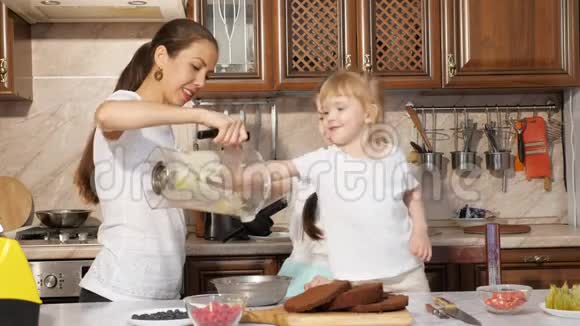 家人妈妈和女儿正在为蛋糕做奶油然后从搅拌机里倒在碗里视频的预览图