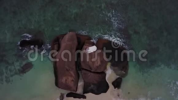 塞舌尔的婚礼仪式结束后情侣们坐在海滩附近的岩石上Drone拍摄了4K视频的预览图