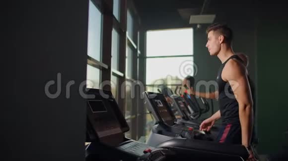 男人在健身室里踩着跑步机走路一群人走在跑步机上靠近一个大的全景窗口开始视频的预览图
