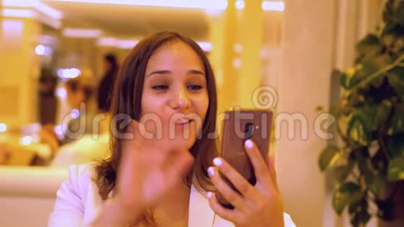 快乐的年轻女子使用智能手机在线视频呼叫酒店餐厅微笑的女人在网上打视频电话视频的预览图