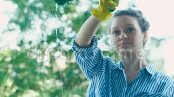 年轻女子在肮脏的窗户上用绿色的湿海绵刮擦器视频的预览图
