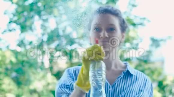 年轻女子的剪影在肮脏的窗户上喷洒洗涤剂视频的预览图