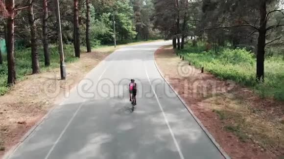 身穿粉色运动衫头戴黑色头盔的年轻迷人的白人女子正在夏日森林里骑自行车无人机sh视频的预览图