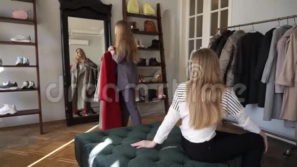两个女孩或双胞胎姐妹一起购物长头发的金发年轻女性正在尝试新的灰色和红色外套而视频的预览图
