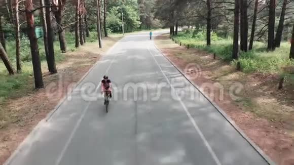 年轻迷人的运动女子穿着粉红色的运动衫和黑色的头盔正在夏天的森林里享受她骑自行车的乐趣医生视频的预览图