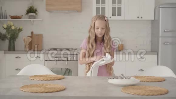 年轻严肃的白人少女穿着粉色连衣裙在现代厨房擦盘子年轻的金发女郎视频的预览图