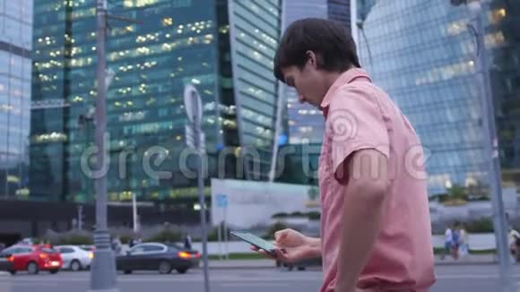 年轻的帅哥使用智能手机在大工业大厦旁行走视频的预览图