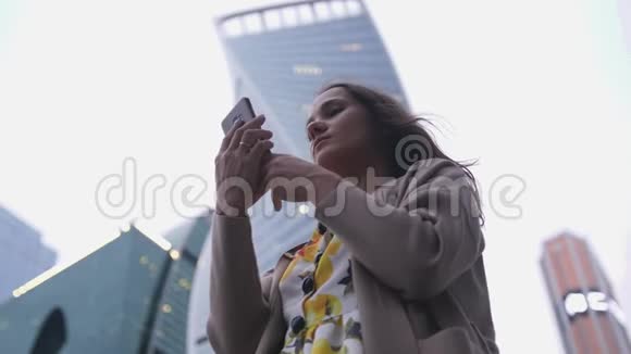 有魅力的女人在建筑物和天空的背景下谈论手机视频的预览图