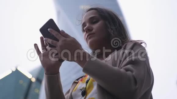 漂亮的黑发女人在建筑物和天空的背景下使用手机视频的预览图