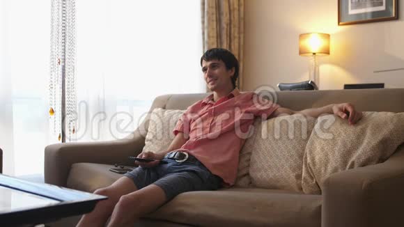 帅哥坐在沙发上在家看电视上的喜剧系列视频的预览图