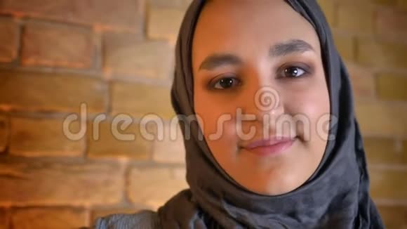 年轻可爱的穆斯林女青年戴着头巾直视镜头在舒适的室内开心地微笑的特写镜头视频的预览图
