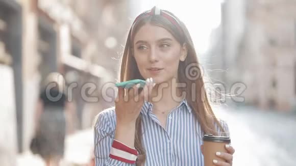美丽的微笑年轻女性棕色头发头戴条纹衬衫用她的智能手机制造声音视频的预览图