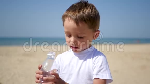 一个孩子在阳光明媚的沙滩上从透明的塑料瓶中喝水视频的预览图