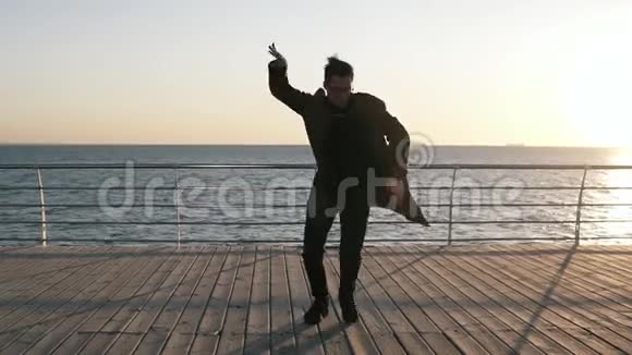 一位年轻的流行歌手穿着深色休闲服装在夏天的木桥上跳舞展示自由泳海滨太阳视频的预览图