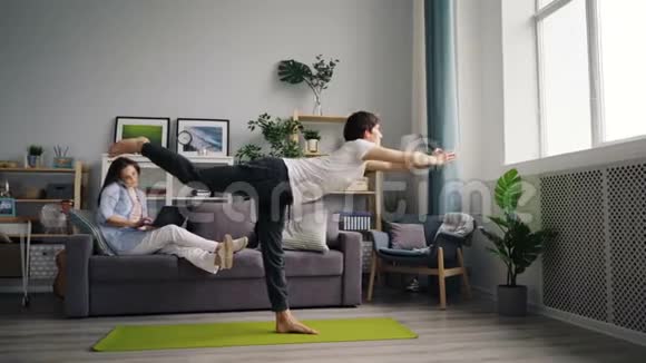 当妻子用手提电脑在手机上说话时亚洲人正在做瑜伽练习视频的预览图