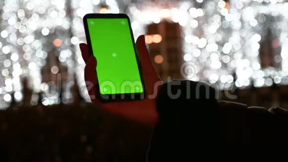 晚间白种人女性双手水平举着绿色屏幕的智能手机视频的预览图