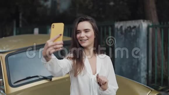 年轻的黑发女孩微笑美丽的女孩结束视频电话通过她的智能手机挥手告别户外年轻女孩视频的预览图