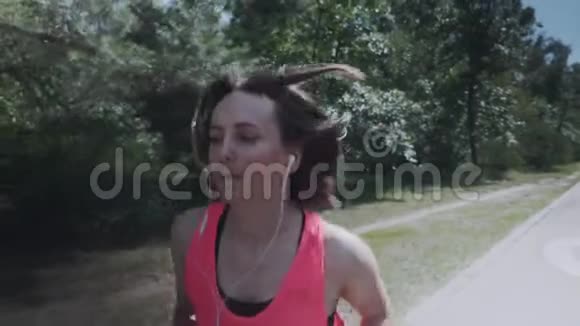 穿着粉红色衬衫在森林里奔跑的迷人的运动女孩苗条的女人有训练有素的身体做运动戴耳机的女孩是不是视频的预览图
