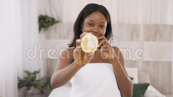 微笑着美丽的年轻非洲女人手里拿着猕猴桃和柠檬片在水疗中心的灯光背景下健康视频的预览图