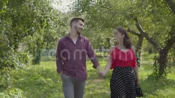 恋爱中的年轻夫妇牵着手在花园里散步快乐的男人和女人在户外视频的预览图